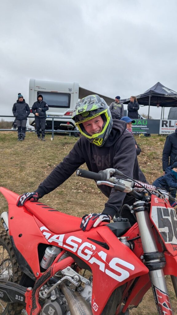 Lachender Motocross-Fahrer mit Helm an seinem Motorrad im Fahrerlager am Echoberg in Tessin